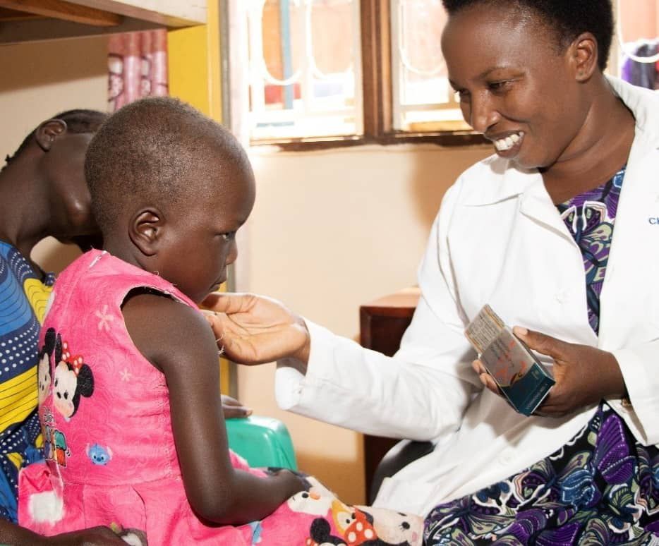Nurse smiling with a young girl receiving treatment while her mother sits beside her