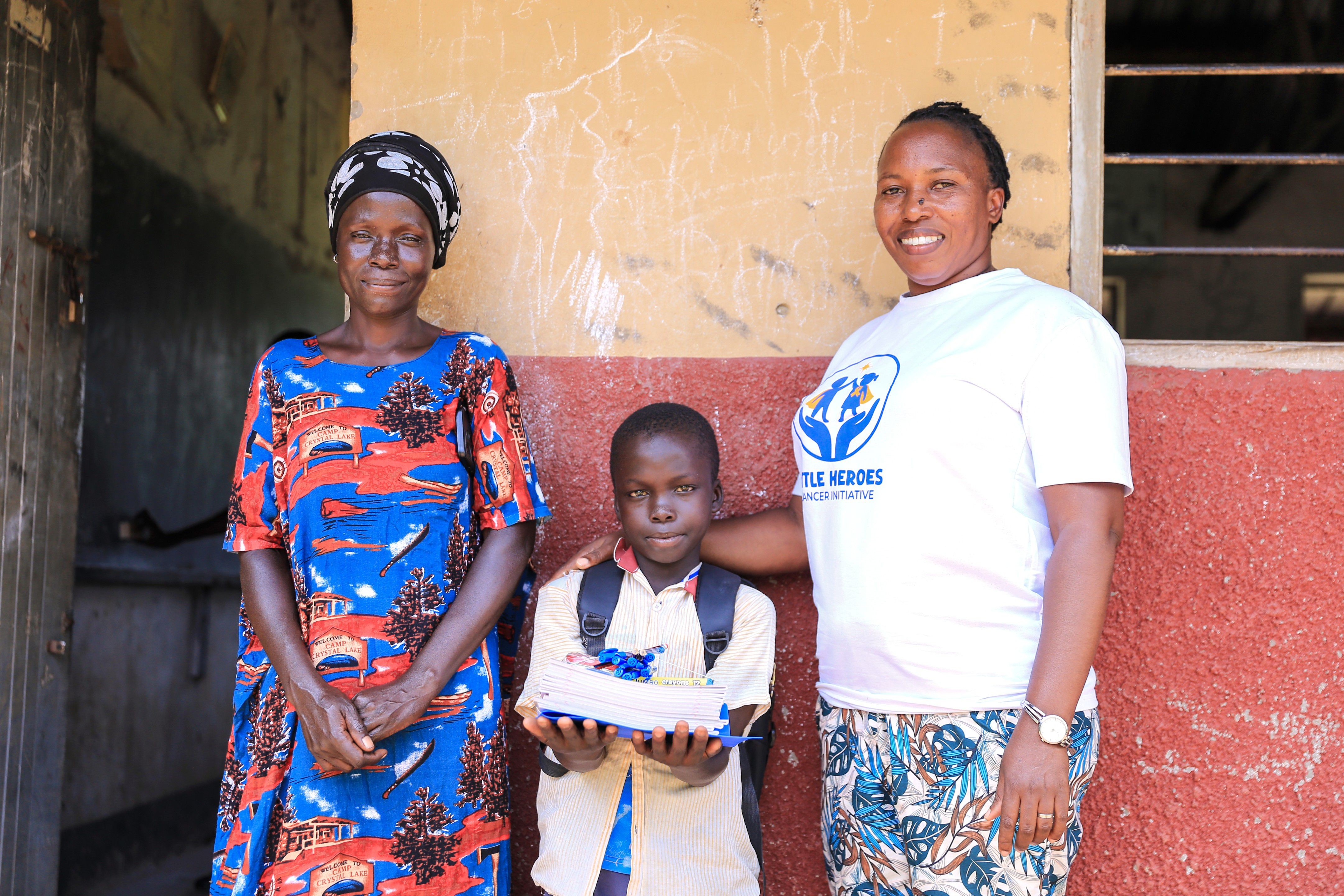A child receiving school materials with a caregiver and Little Heroes team member