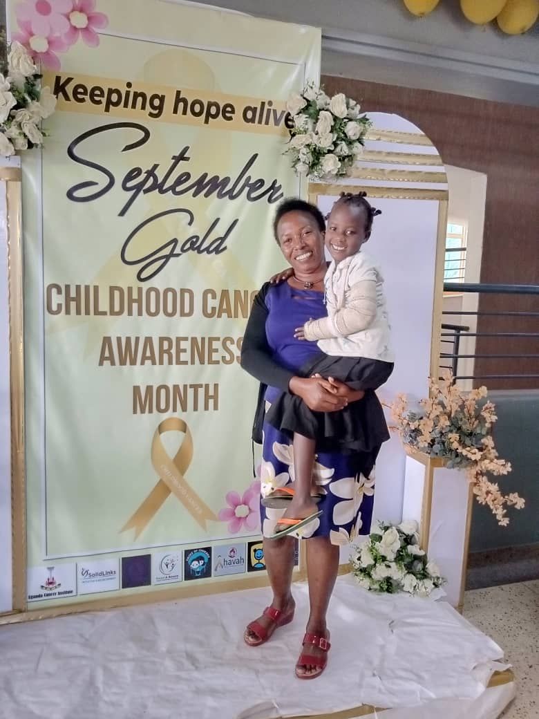 Mother holding a child in front of a September Gold childhood cancer awareness banner